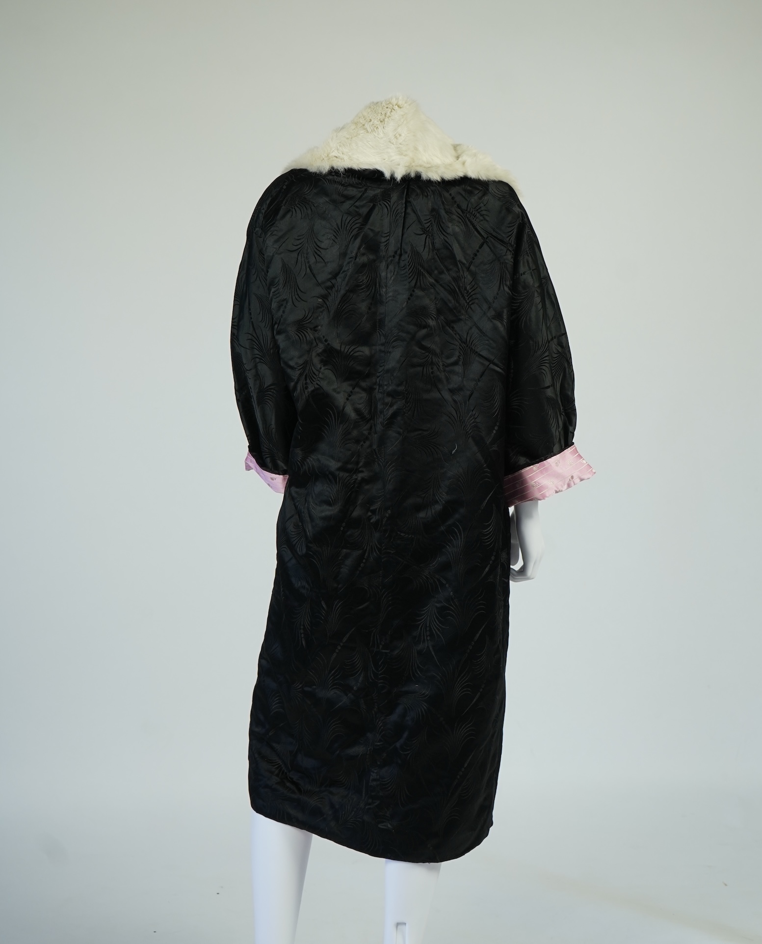 A 20th century ladies black silk damask opera coat, trimmed with a white fur collar and pink silk stripe brocade lining. 116cm from shoulder to hem. Condition - seams unstitched in places, small nick to black brocade by